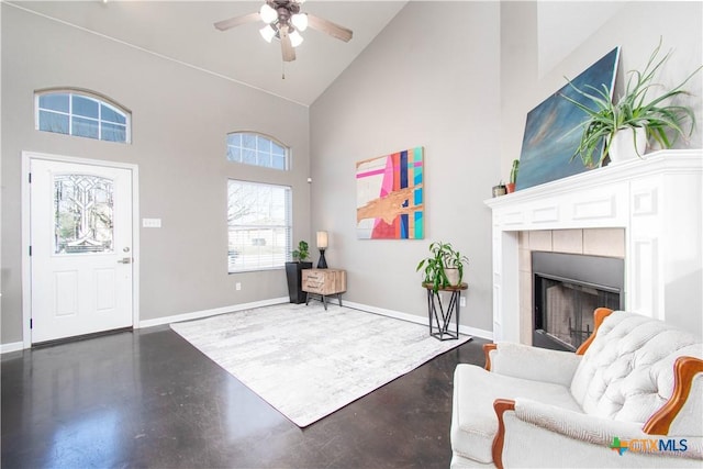 interior space featuring baseboards, a ceiling fan, a tile fireplace, finished concrete floors, and high vaulted ceiling