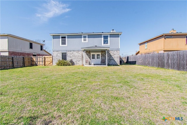 rear view of property featuring a yard, brick siding, a fenced backyard, and french doors