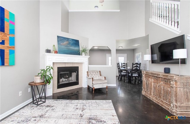 living room with a high ceiling, a tile fireplace, and baseboards