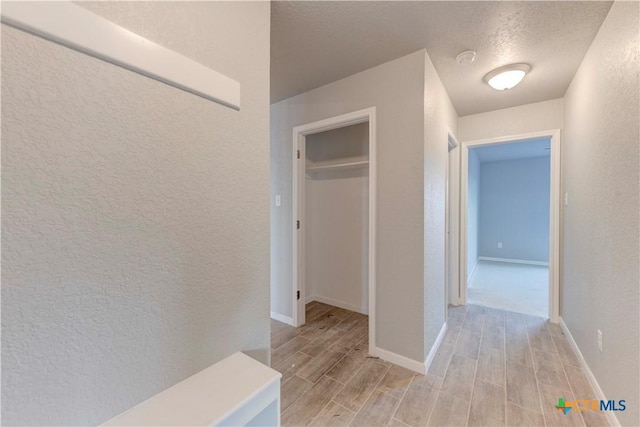 hall featuring wood tiled floor, a textured wall, a textured ceiling, and baseboards