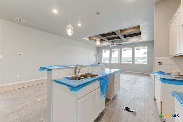 kitchen with visible vents, coffered ceiling, a sink, a kitchen island with sink, and backsplash