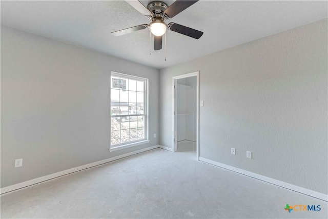 spare room featuring ceiling fan, baseboards, and unfinished concrete floors