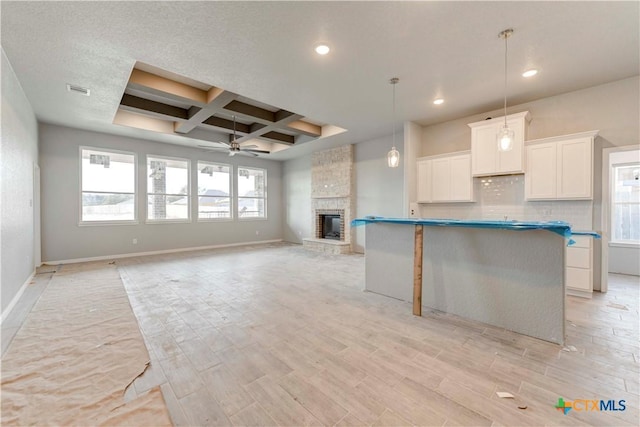 kitchen with white cabinets, decorative backsplash, coffered ceiling, a ceiling fan, and a stone fireplace