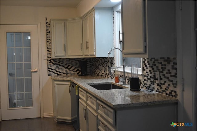 kitchen with sink, decorative backsplash, dark tile patterned floors, stainless steel dishwasher, and light stone counters