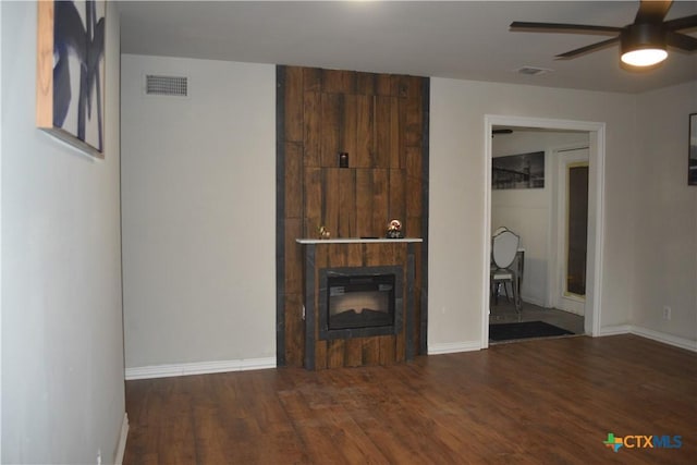 unfurnished living room with dark wood-type flooring, a large fireplace, and ceiling fan