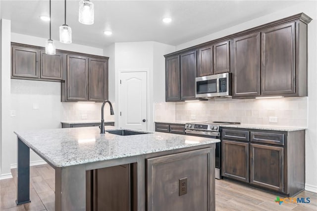 kitchen with pendant lighting, a center island with sink, sink, light stone countertops, and stainless steel appliances