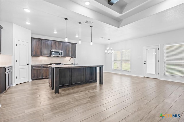 kitchen with a kitchen island with sink, dark brown cabinets, pendant lighting, and an inviting chandelier