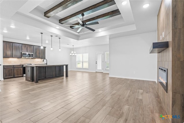 living room with ceiling fan with notable chandelier, a large fireplace, a tray ceiling, and sink