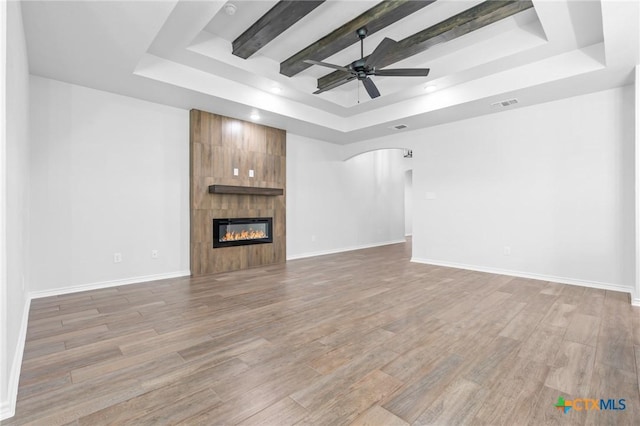 unfurnished living room featuring beam ceiling, a raised ceiling, ceiling fan, and a tiled fireplace