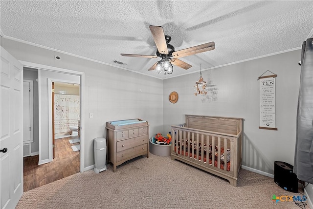 carpeted bedroom featuring ornamental molding, a textured ceiling, ceiling fan, a nursery area, and connected bathroom