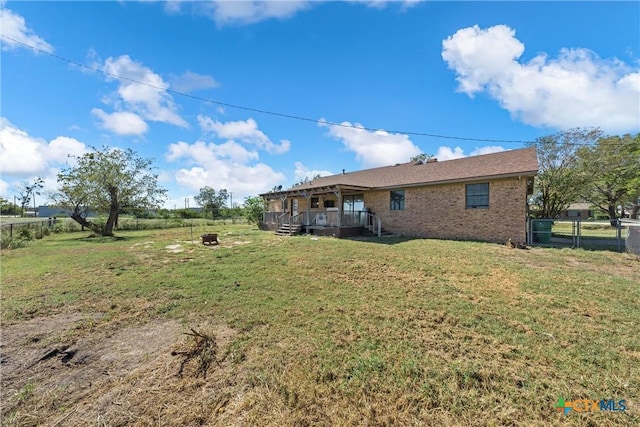 back of property with a deck, an outdoor fire pit, and a yard