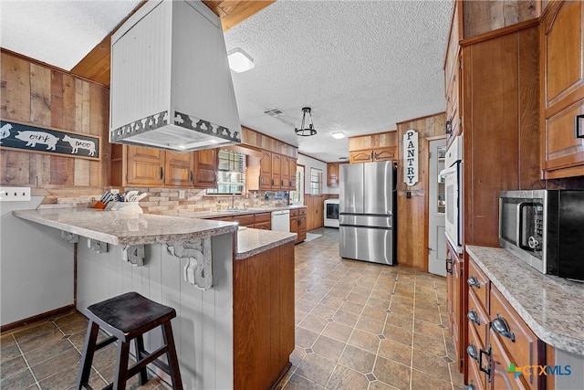 kitchen featuring wood walls, a kitchen breakfast bar, a textured ceiling, appliances with stainless steel finishes, and kitchen peninsula