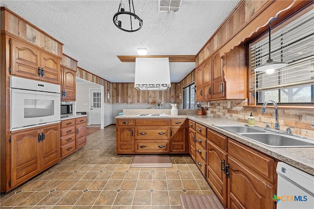 kitchen featuring sink, backsplash, kitchen peninsula, white appliances, and decorative light fixtures