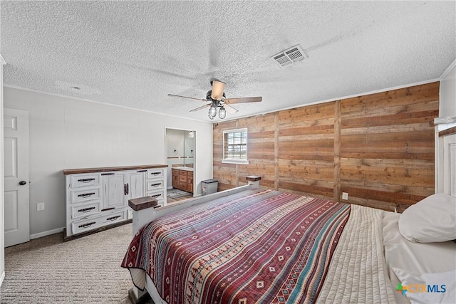 bedroom with ensuite bath, ceiling fan, wood walls, light colored carpet, and a textured ceiling