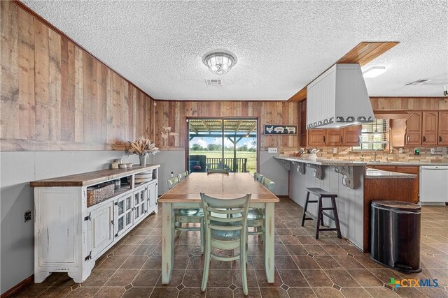 kitchen featuring dishwasher, wood walls, a breakfast bar, a textured ceiling, and tasteful backsplash