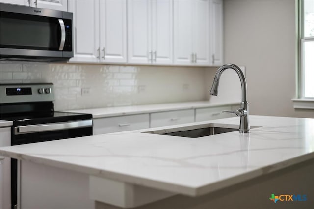 kitchen with light stone counters, white cabinetry, sink, and appliances with stainless steel finishes