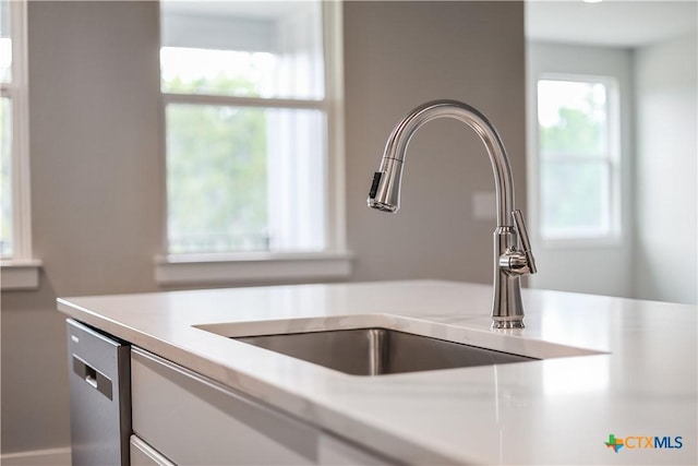 interior details with a sink, stainless steel dishwasher, white cabinets, and light countertops