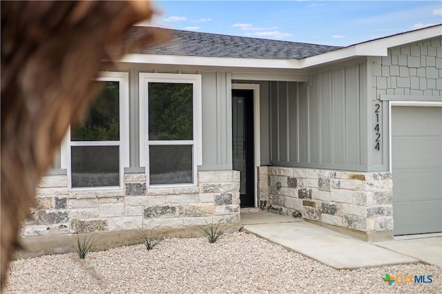 entrance to property featuring a garage, stone siding, and a shingled roof