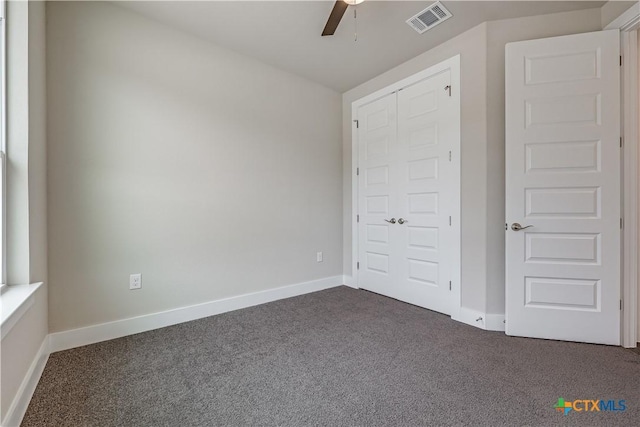 unfurnished bedroom featuring visible vents, baseboards, a ceiling fan, and dark carpet