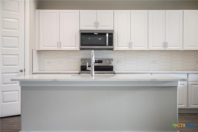 kitchen with stainless steel appliances, tasteful backsplash, an island with sink, and white cabinetry