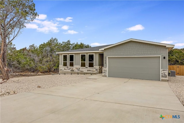 view of front of property with fence, central AC, a garage, stone siding, and driveway