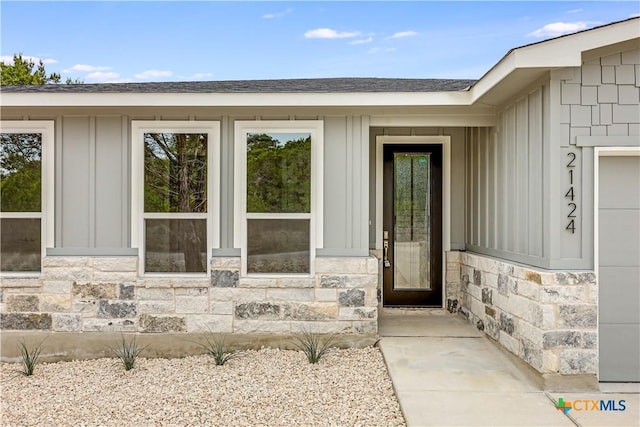 property entrance featuring board and batten siding, stone siding, and roof with shingles