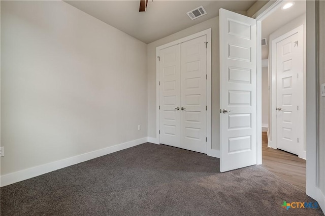 unfurnished bedroom with a closet, visible vents, dark carpet, and baseboards