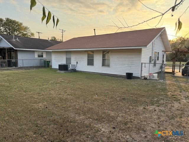 back house at dusk featuring cooling unit and a yard