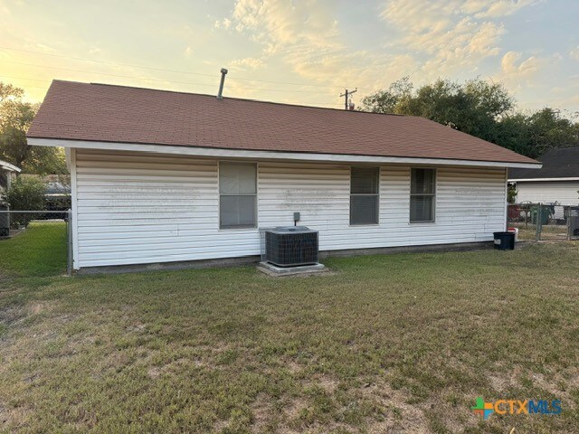 back house at dusk with central AC and a yard