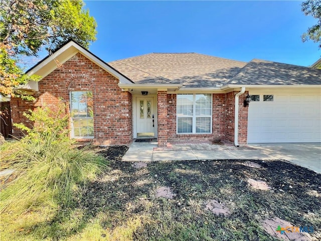 single story home with a shingled roof, a garage, concrete driveway, and brick siding