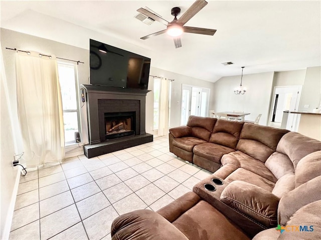 living area featuring a brick fireplace, ceiling fan with notable chandelier, vaulted ceiling, and light tile patterned floors