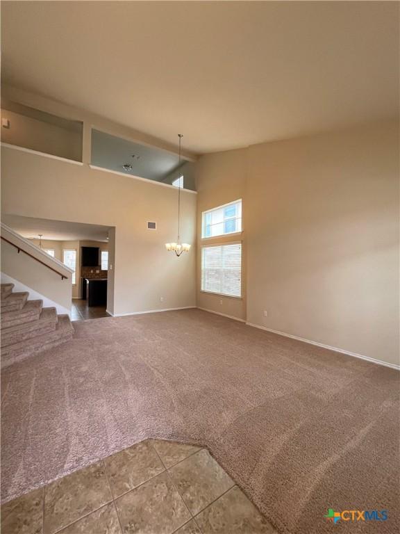 unfurnished living room with carpet floors, a chandelier, and high vaulted ceiling