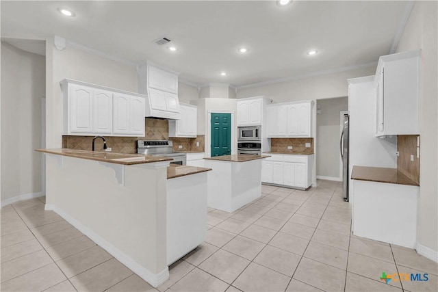 kitchen with stainless steel appliances, a kitchen island, kitchen peninsula, crown molding, and white cabinets