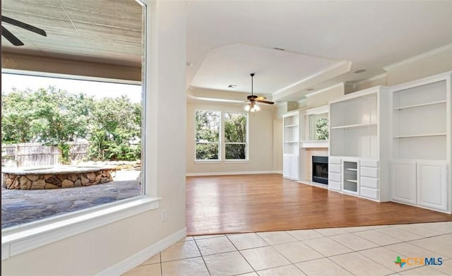 unfurnished living room with light tile patterned floors, a raised ceiling, ceiling fan, and crown molding