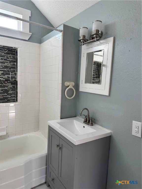 bathroom with lofted ceiling, vanity, tiled shower / bath combo, and a textured ceiling