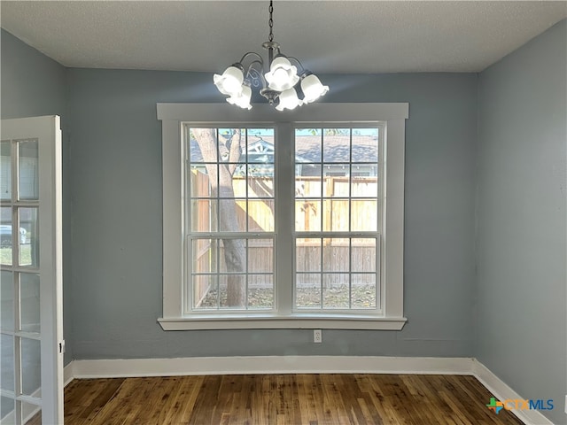 unfurnished dining area with a healthy amount of sunlight, dark hardwood / wood-style flooring, a textured ceiling, and an inviting chandelier