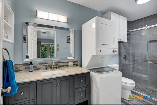 bathroom with toilet, a shower with door, tasteful backsplash, vanity, and stacked washer / drying machine