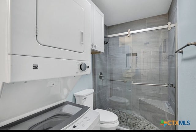 bathroom featuring walk in shower, stacked washer and dryer, and toilet