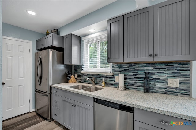 kitchen with stainless steel appliances, light hardwood / wood-style floors, sink, light stone counters, and gray cabinetry