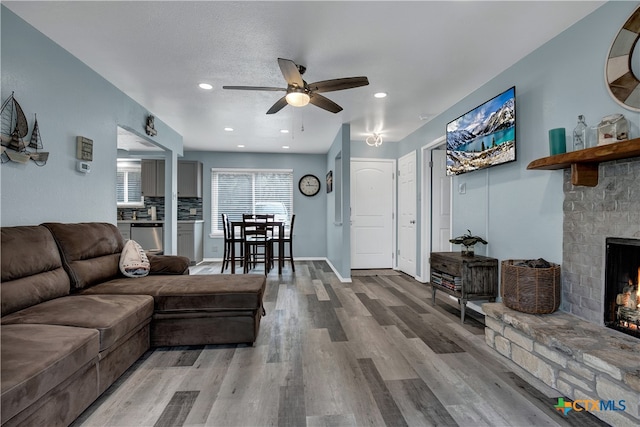 living room with wood-type flooring, ceiling fan, and a fireplace