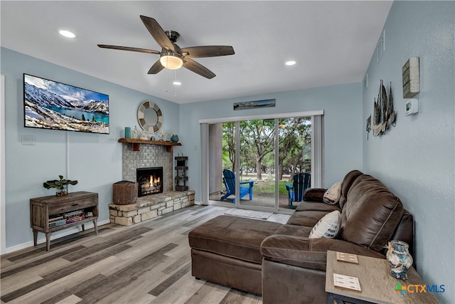 living room featuring a stone fireplace, light wood-type flooring, and ceiling fan