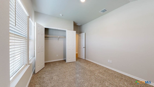 unfurnished bedroom featuring multiple windows, light carpet, a closet, and lofted ceiling