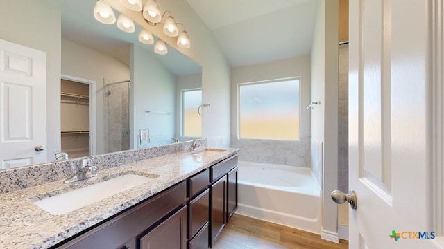 bathroom with hardwood / wood-style flooring, a tub to relax in, vanity, and vaulted ceiling