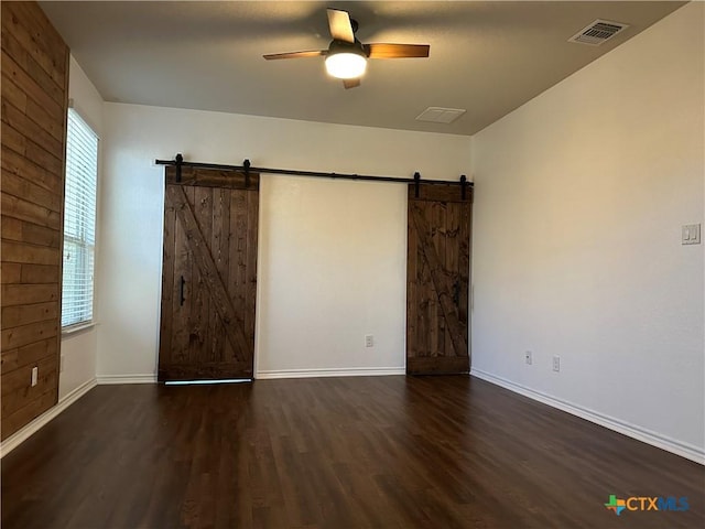 spare room featuring dark hardwood / wood-style floors, a barn door, a healthy amount of sunlight, and ceiling fan