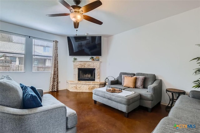 living room featuring ceiling fan, baseboards, and a fireplace with raised hearth