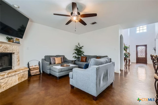 living area with arched walkways, finished concrete flooring, visible vents, ceiling fan, and a stone fireplace