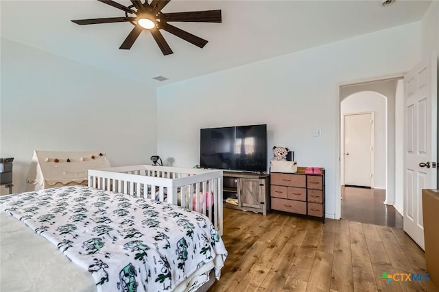 bedroom with arched walkways, ceiling fan, wood finished floors, and visible vents