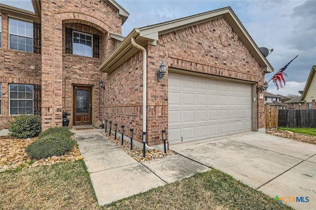 view of front of house with a garage, driveway, brick siding, and fence