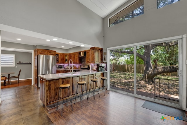 kitchen featuring a breakfast bar, appliances with stainless steel finishes, kitchen peninsula, high vaulted ceiling, and dark wood-type flooring