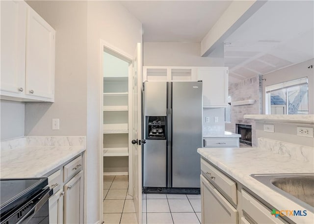 kitchen with light tile patterned floors, white cabinetry, stainless steel fridge, and black electric range